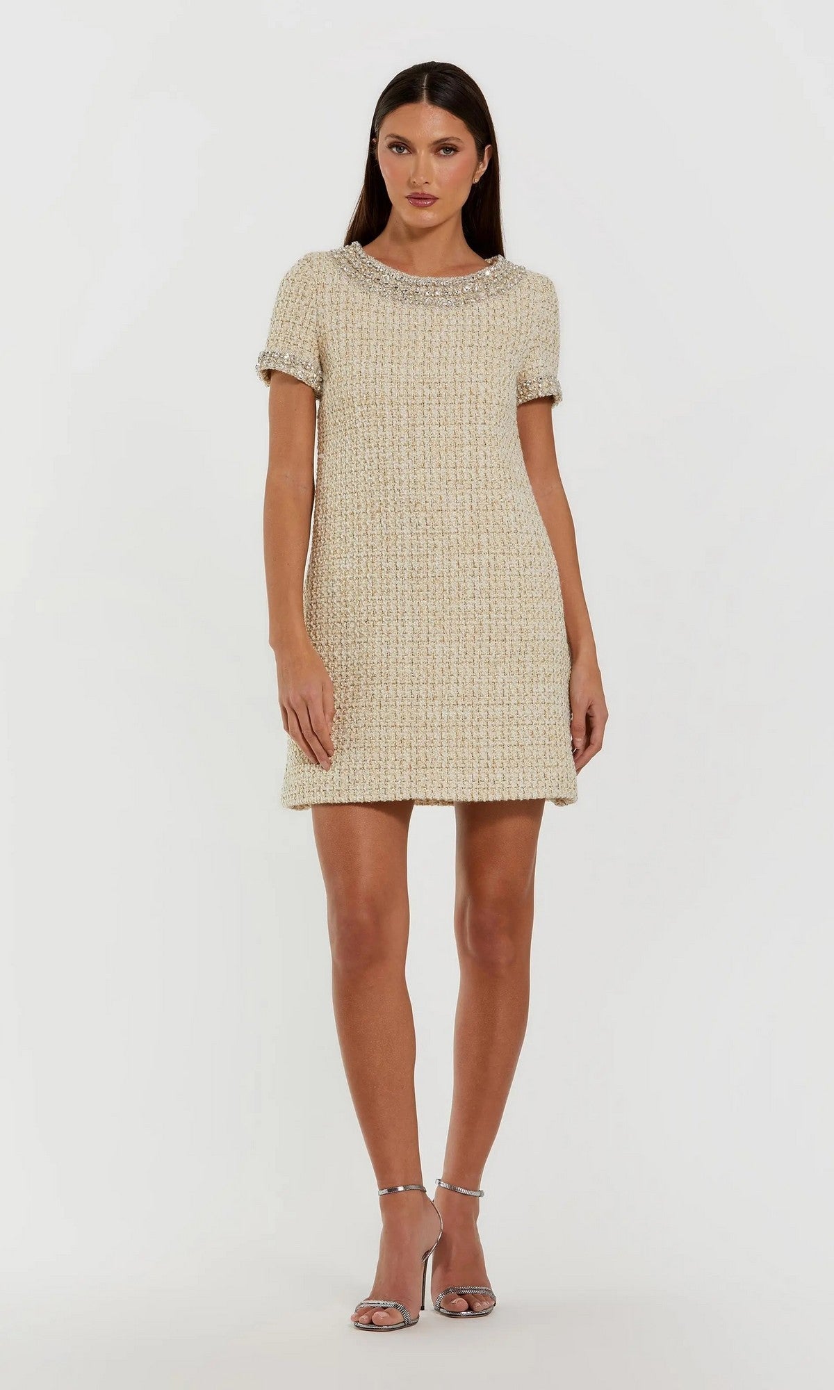 A woman stands against a plain white background wearing the Mac Duggal 37075 short semi-formal dress, featuring cream-colored boucle fabric with delicate rhinestone beading, perfectly styled with silver high-heeled sandals.
